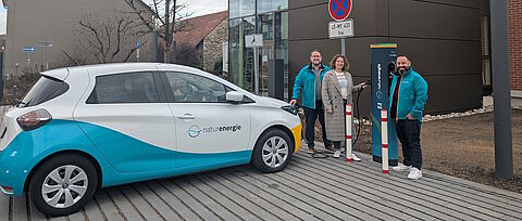 Drei Personen mit E-Auto und Ladesäule