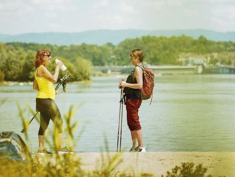 Wanderpause am Rhein mit Blick auf das Wasserkraftwerk Rheinfelden Zwei Damen mit Wanderstöcken und Freizeitkleidung machen eine Pause vor dem Rhein, im Hintergrund das Wasserkraftwerk von Rheinfelden.