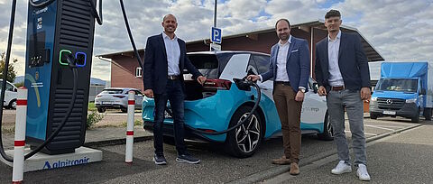 Drei Männer mit Elektro-Auto an Ladesäule
