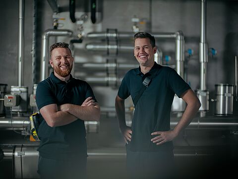 Zwei lachende Männer stehen in einer technischen Anlage