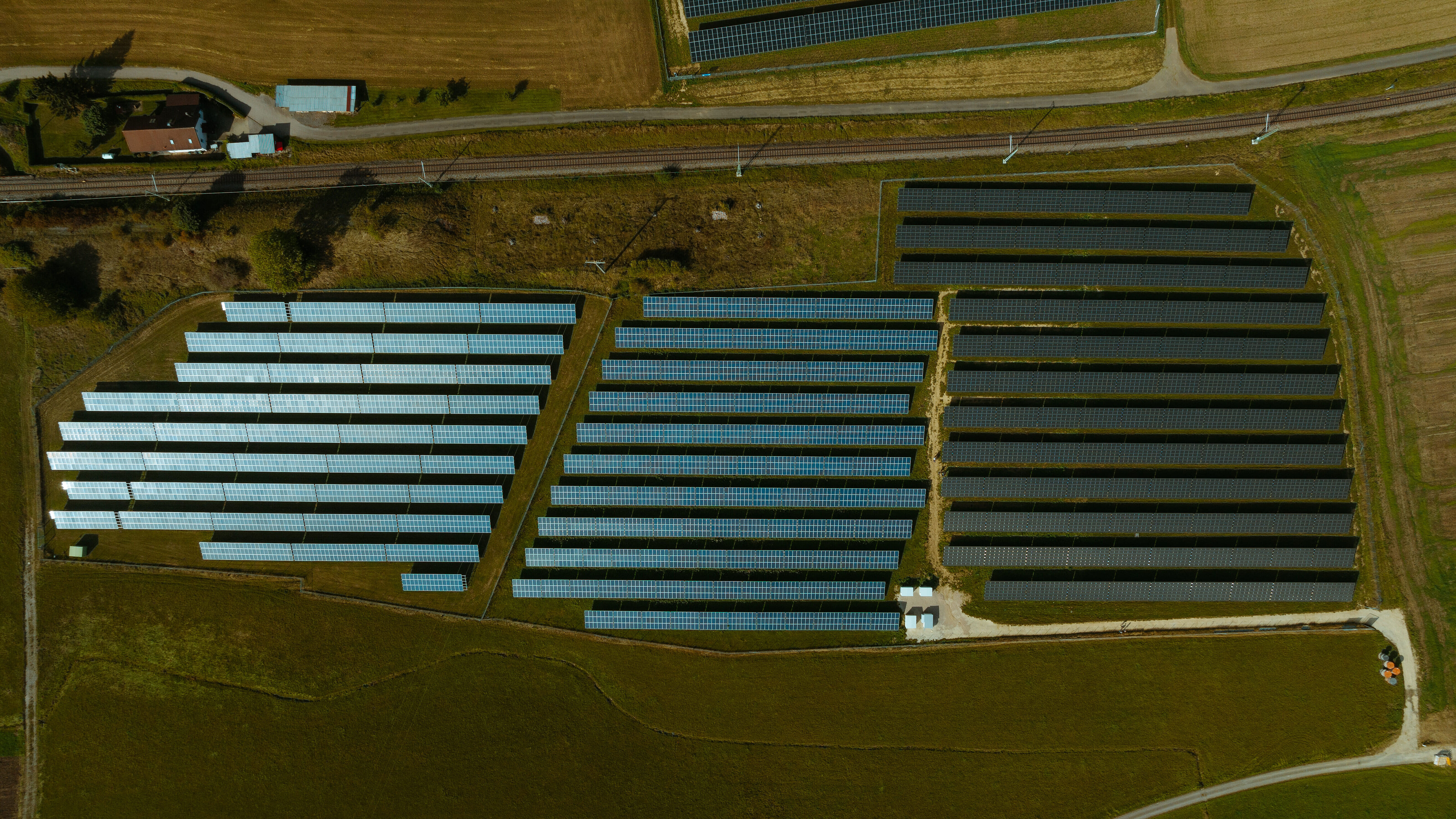 Luftaufnahme einer Solaranlage von naturenergie in Döggingen, bestehend aus mehreren Reihen von Solarpaneelen, die sich über eine große Fläche erstrecken. Umgeben von Feldern und einer Eisenbahnlinie.