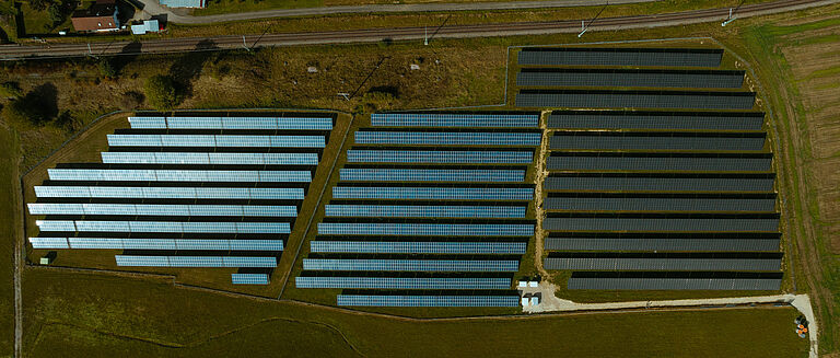 Luftaufnahme einer Solaranlage von naturenergie in Döggingen, bestehend aus mehreren Reihen von Solarpaneelen, die sich über eine große Fläche erstrecken. Umgeben von Feldern und einer Eisenbahnlinie.