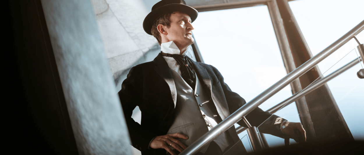 Ein elegant gekleideter Mann in einem schwarzen Anzug und Hut geht eine Treppe hinauf.