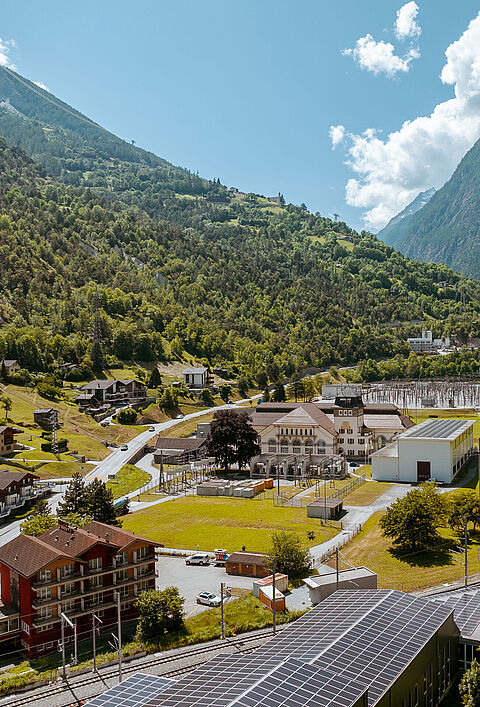Tal mit Fluss, rotem Zug und Solaranlage auf Gebäudedach und Kraftwerk.