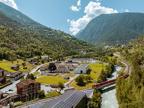 Tal mit Bahn, Fluss und Solaranlage Tal mit Fluss, rotem Zug und Solaranlage auf Gebäudedach und Kraftwerk.
