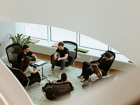Drei naturenergie-Mitarbeiter stehen in einem Büro und besprechen ein Projekt. Sie sind in einem hellen Raum mit großen Fenstern und arbeiten gemeinsam an einem Computer.
