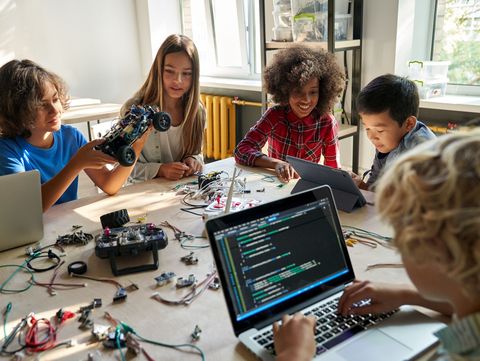 Eine Gruppe von jungen Menschen arbeitet gemeinsam an einem Tisch mit technischen Geräten und Laptops. Sie bauen und programmieren ein Modellauto und andere elektronische Projekte.