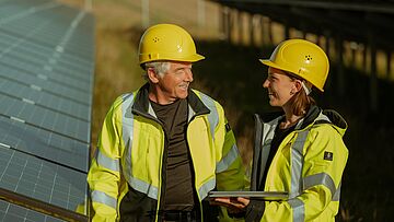 Mitarbeitende im Solarpark auf Freifläche Zwei Personen in Arbeitskleidung stehen im Solarpark auf einer Freifläche