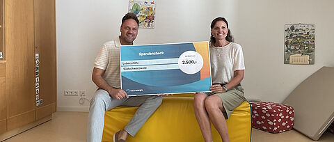 Mann und Frau sitzend mit Spendenscheck