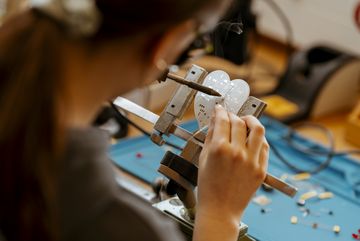 Girlsday: Ein Mädchen mit langen Haaren arbeitet an einer technischen Vorrichtung, die eine Herzform hat. Sie verwendet ein Werkzeug, um präzise Löcher in das Material zu bohren