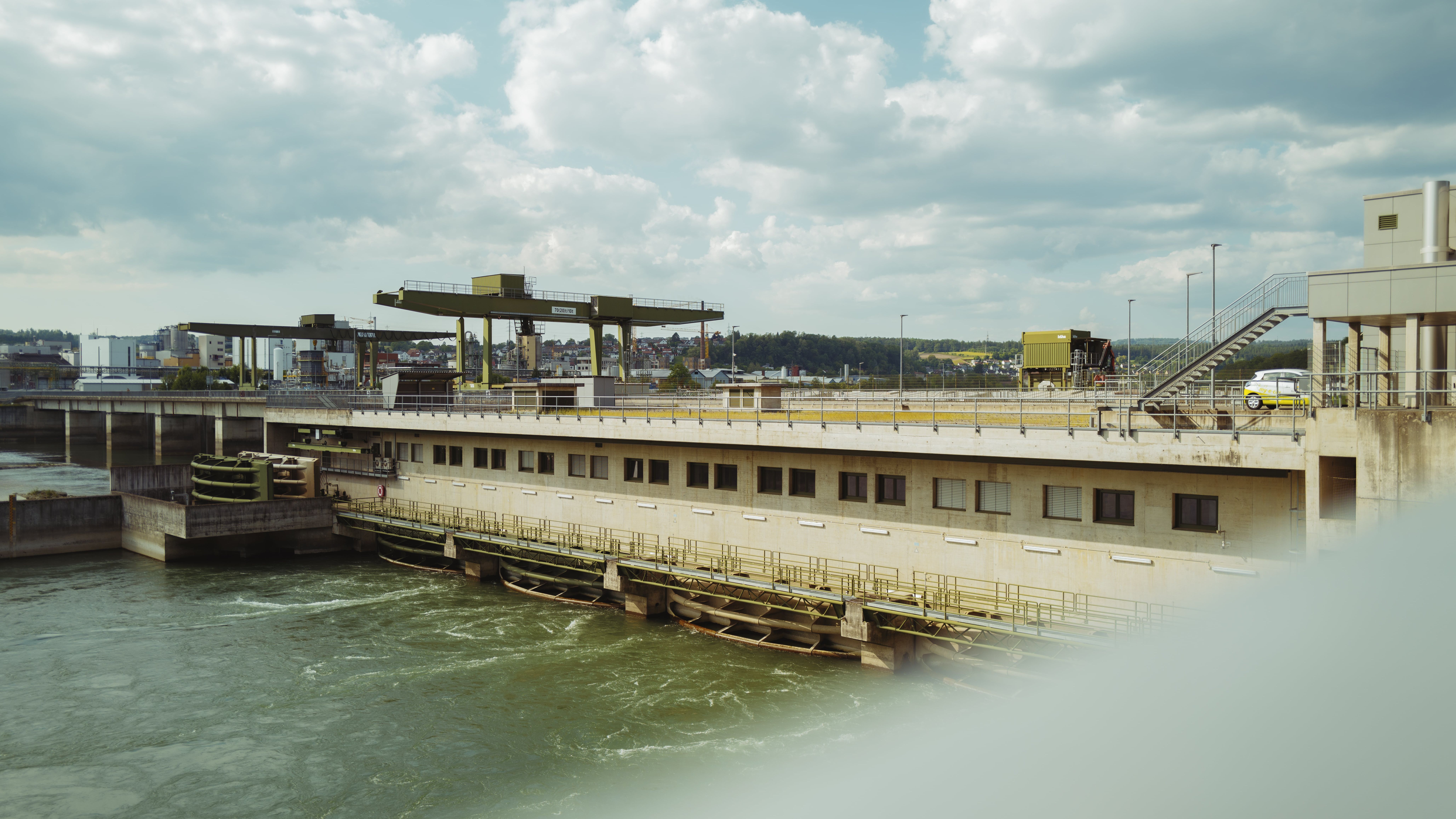 Ein modernes Wasserkraftwerk von naturenergie im Raum Südbaden, das nachhaltigen Strom produziert. Im Vordergrund sind die Turbinen und die Struktur des Kraftwerks zu sehen, während im Hintergrund die umliegende Landschaft und Gebäude sichtbar sind