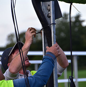 Personen befestigen schwarze DC‑Kabel an einem Metallpfosten der Unterkonstruktion eines Freiflächen‑Solarparks.