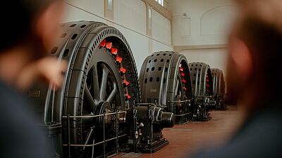 Große Turbinen in einem Wasserkraftwerk, mit roten Akzenten auf den Rädern, in einer geräumigen Halle.
