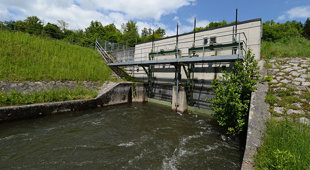 3.	Das Bild zeigt das Wasserkraftwerk in Steinen Es ist eine moderne Anlage mit einem Wasserkanal, der durch ein Betonbauwerk fließt. Im Hintergrund sind grüne Wiesen und Bäume zu sehen.